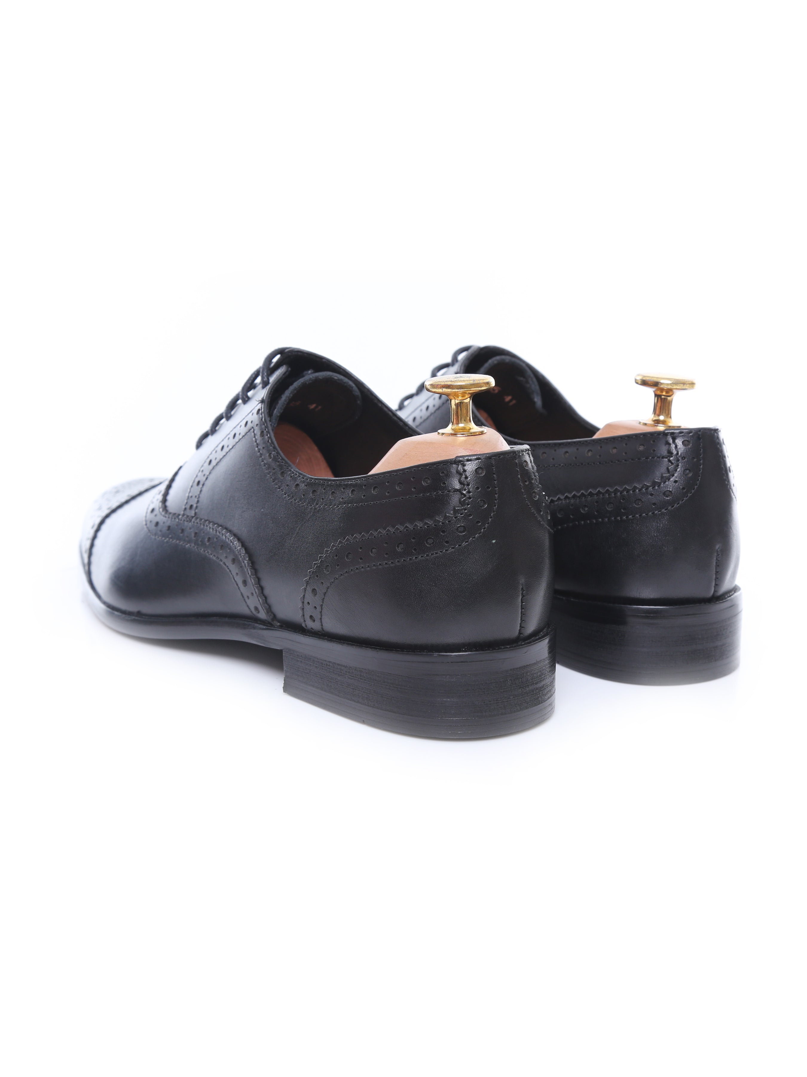 Pair of black leather men’s dress shoes with brogue detailing and shoe trees, rear view