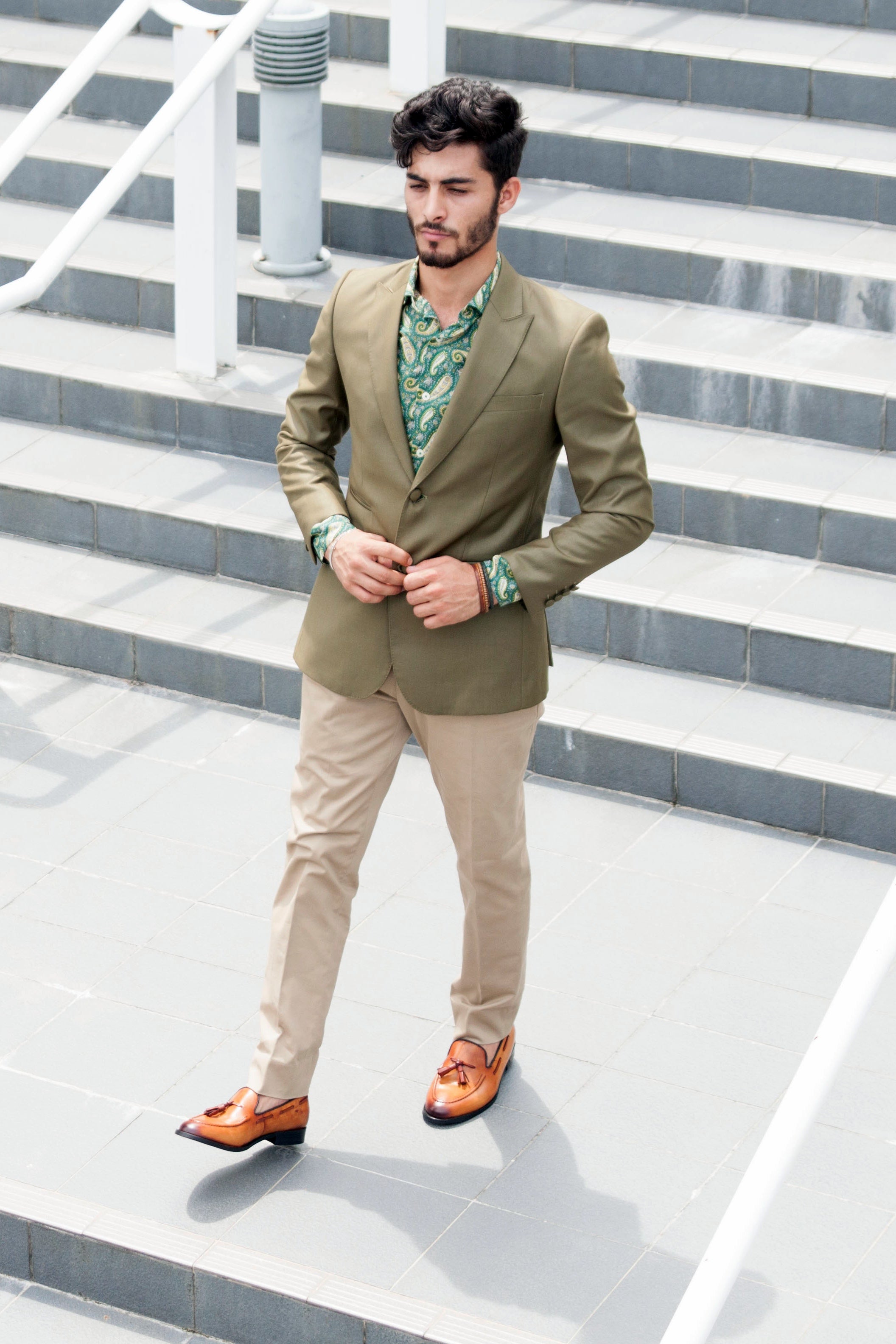 Man wearing olive blazer, paisley shirt, beige pants, and tan loafers outdoors on steps