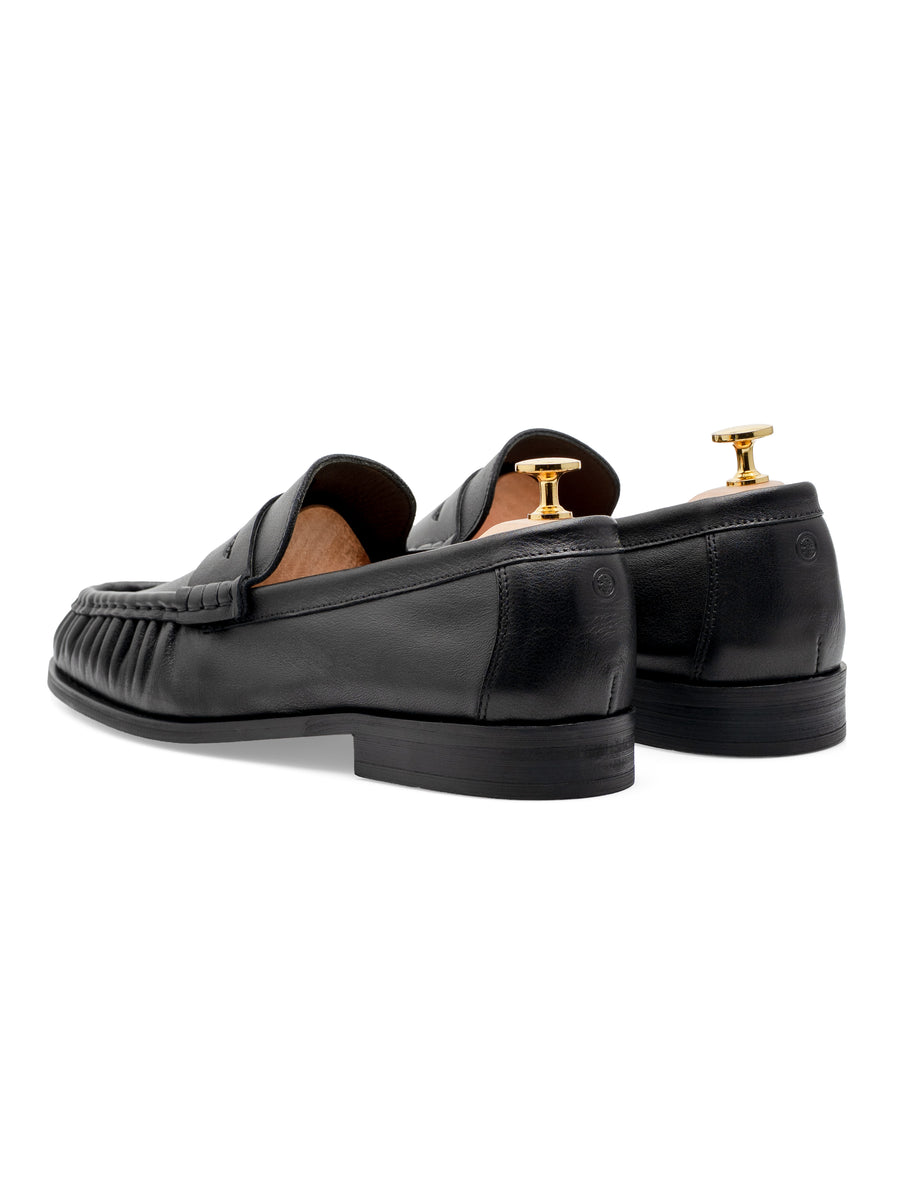 Black leather loafers with tassel detail and gold shoe trees, ideal for formal or smart casual wear.