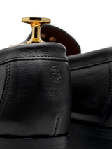 Black leather loafer with gold shoe tree, showcasing detailed stitching and embossed logo