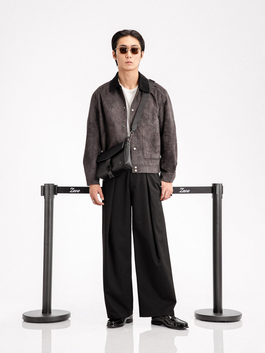 Man in stylish black loafers, wide-leg pants, and suede jacket with crossbody bag, sunglasses, minimalist studio setting