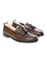 Handmade men's brown fringe tassel leather loafers with patina finish on white background