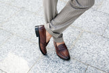 Brown leather loafers with pinstripe trousers on stone pavement