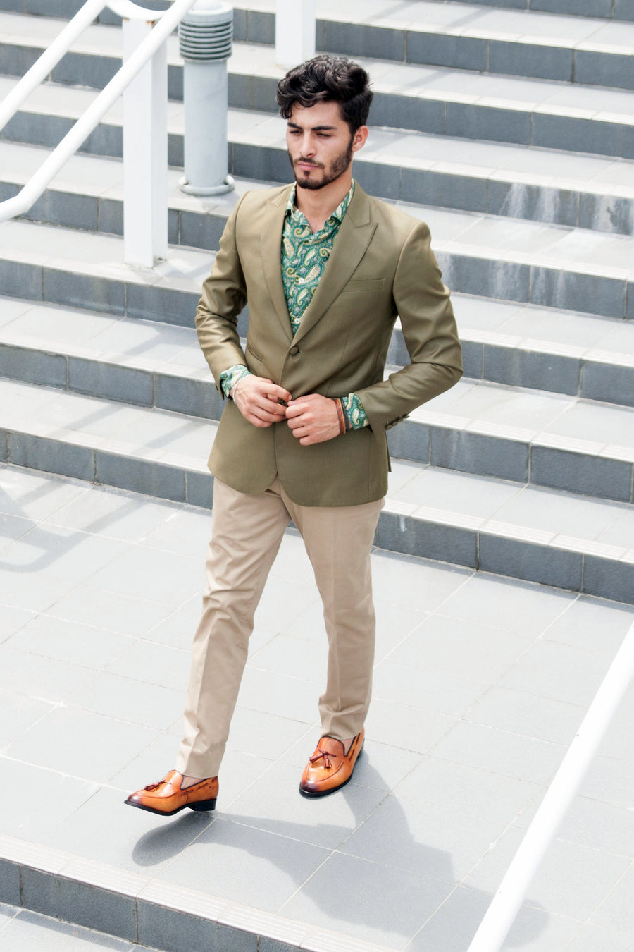 Man wearing olive blazer, paisley shirt, beige pants, and tan loafers outdoors on steps